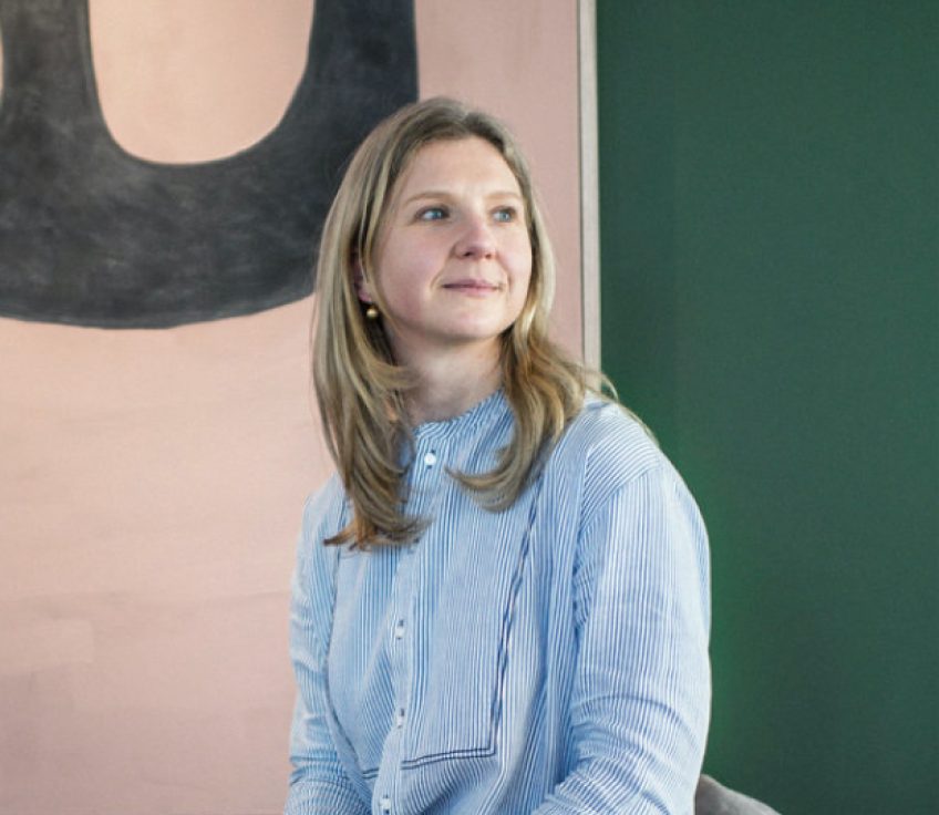 Iva Foschia in blue striped shirt sitting in front of abstract wall art.