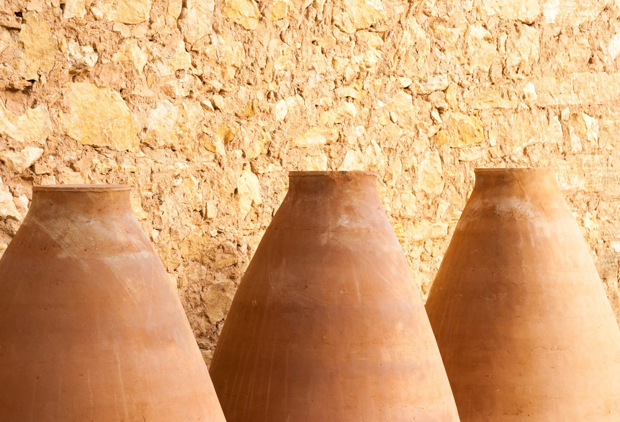 Three large clay jars against a textured stone wall featured in Apivita.