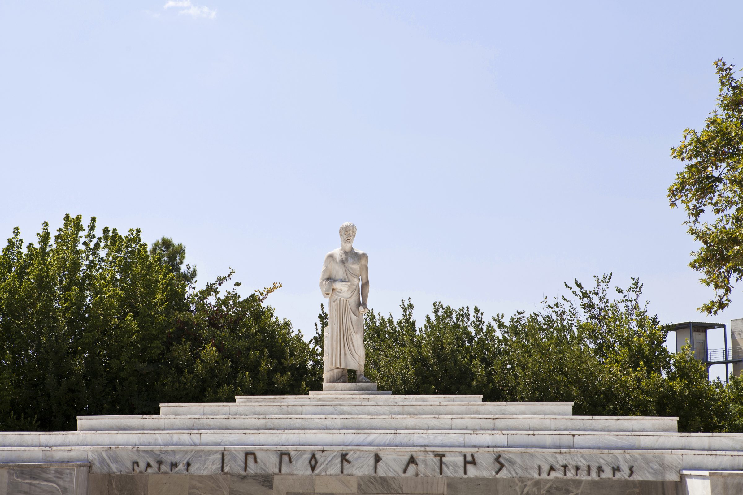 Statue of Hippocrates surrounded by greenery under a clear sky, part of Apivita.