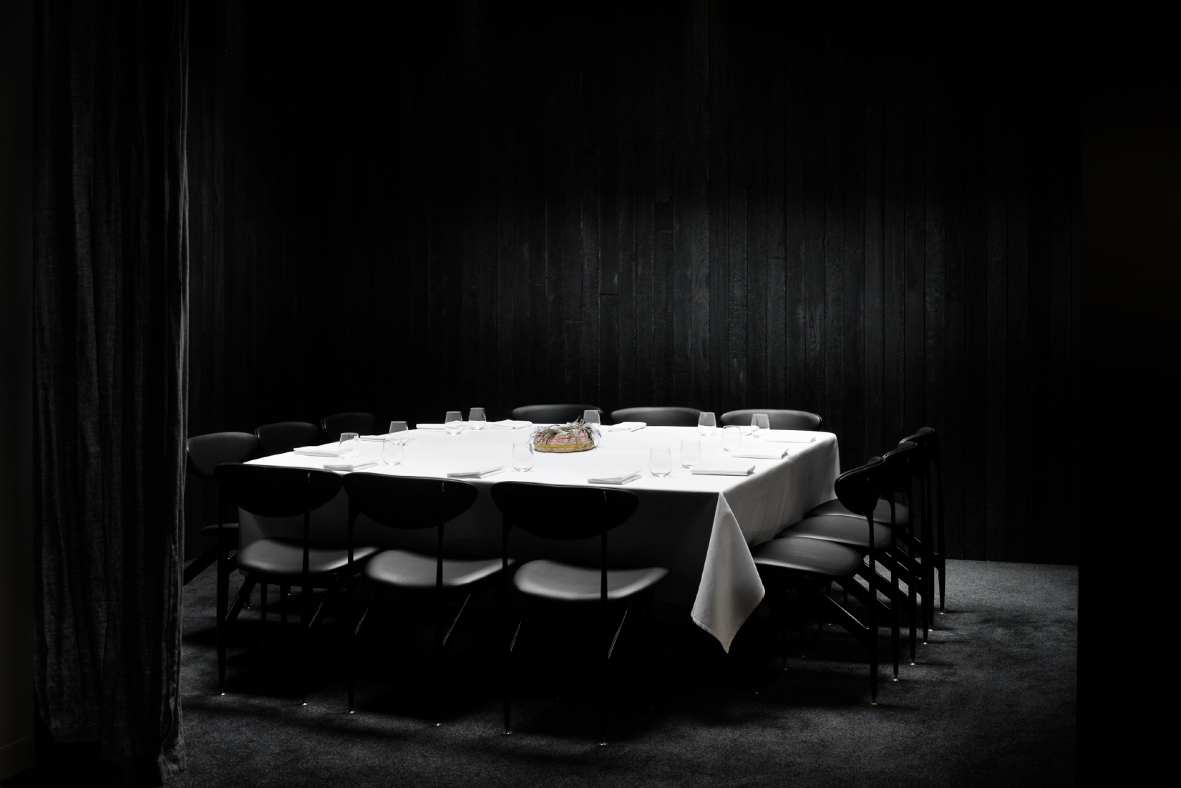 A dimly lit dining room features a square table set for eight from Attica.