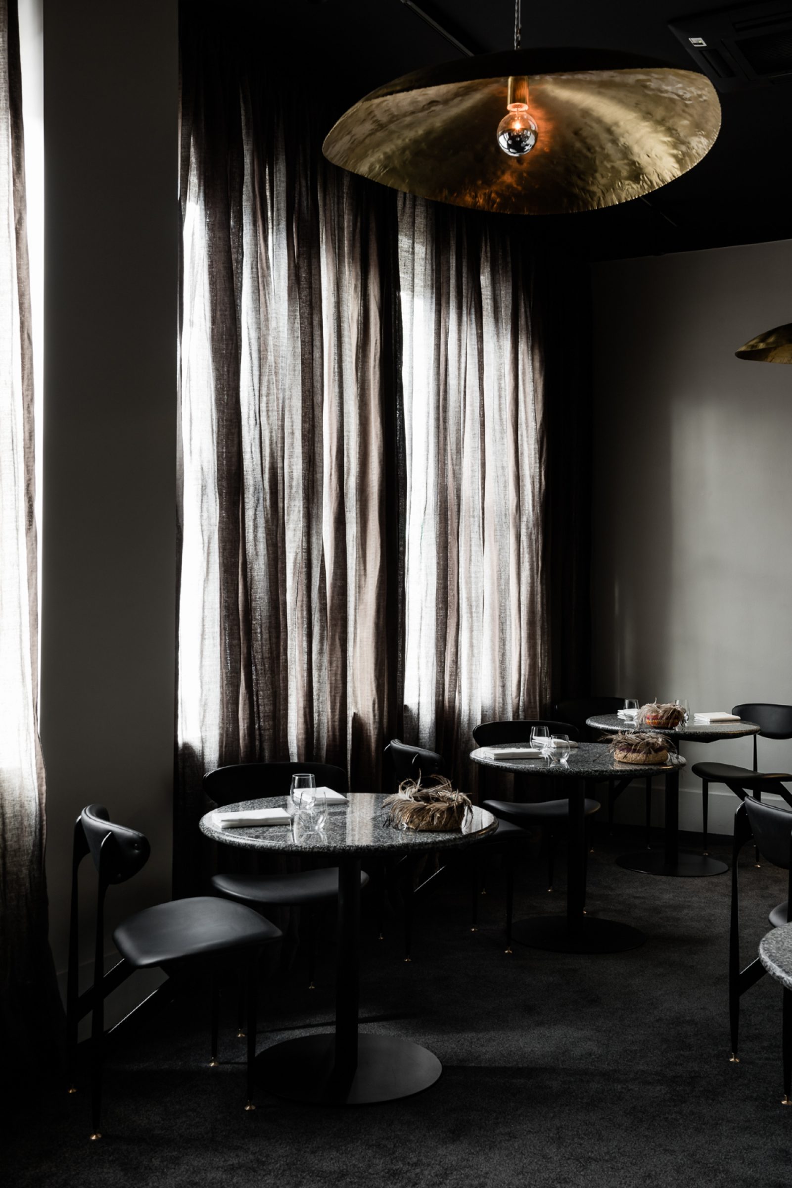 Dimly lit modern dining area with black tables and chairs from Attica project.