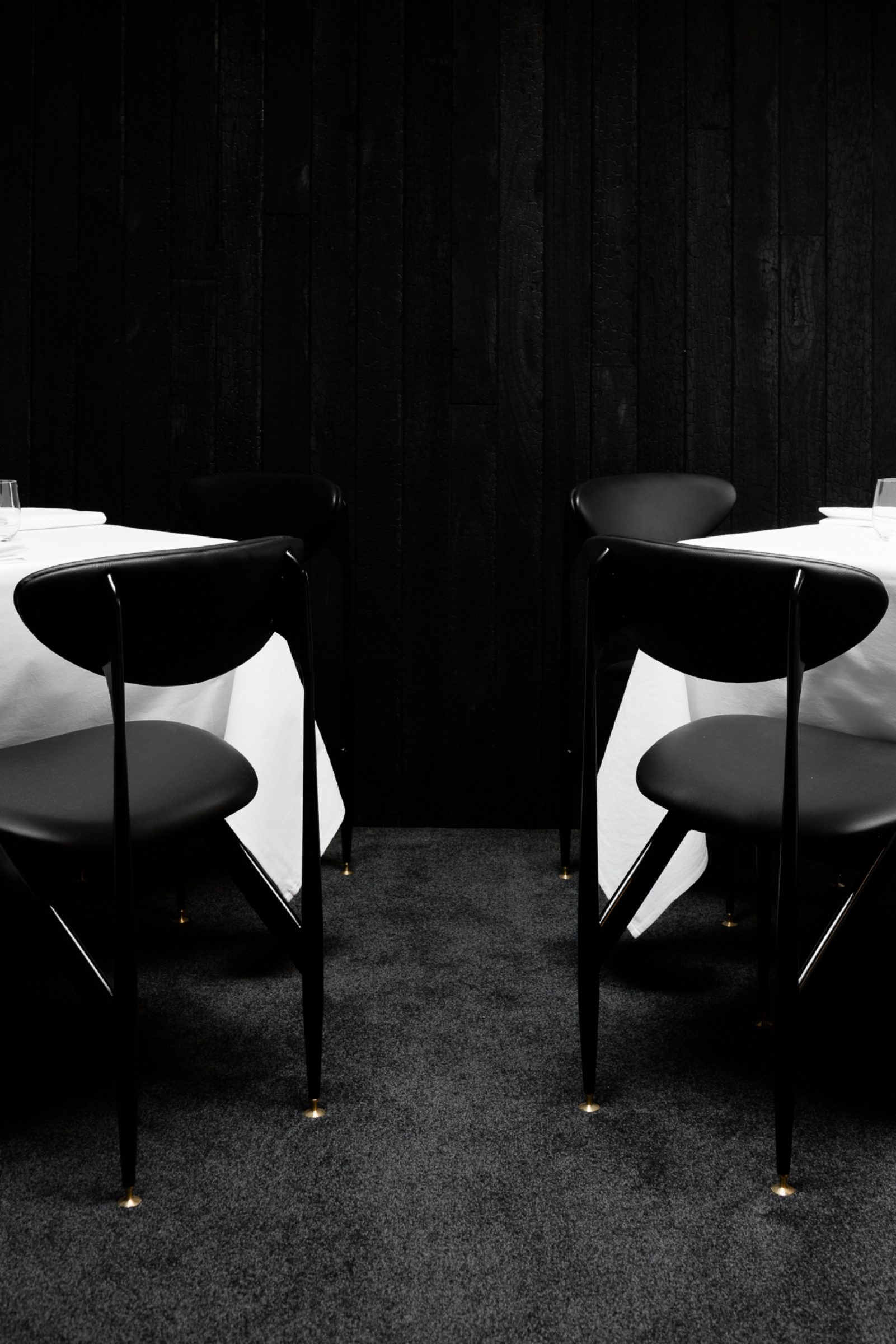 Black chairs and white tablecloths in a dimly lit dining setting from Attica.