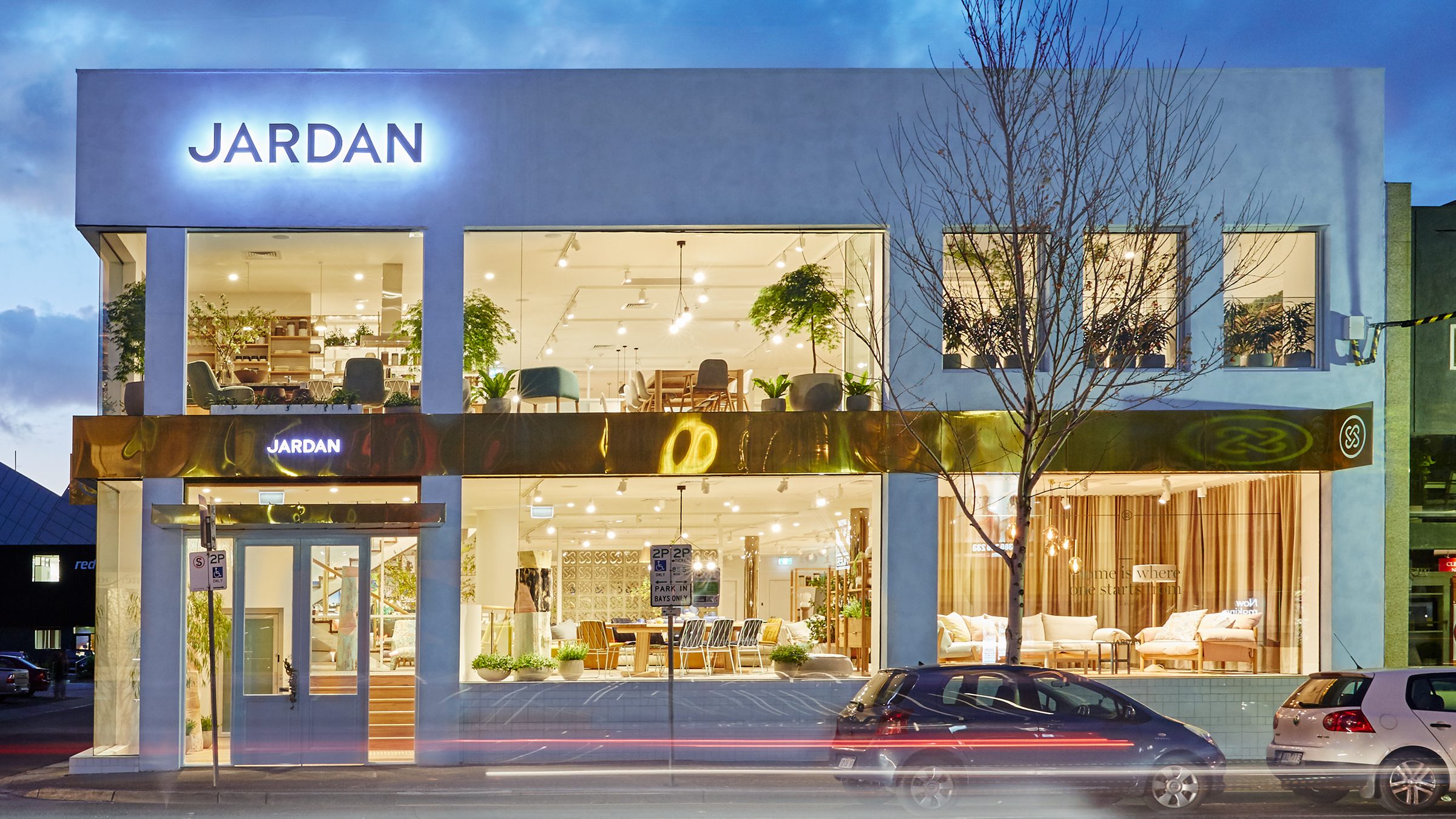 Jardan Melbourne showroom exterior at dusk, showcasing modern furniture and vibrant lighting.