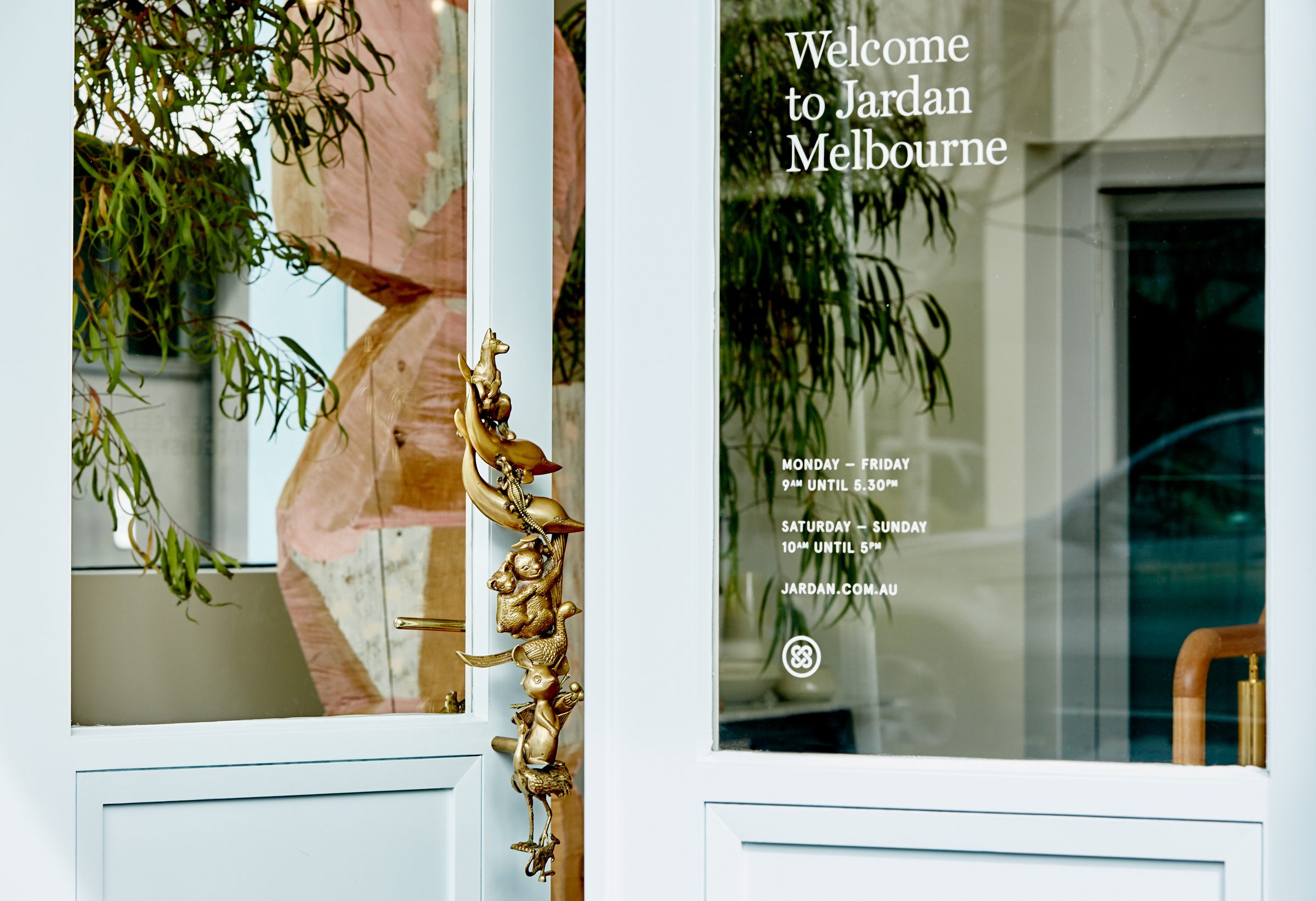 Entrance to Jardan Melbourne with decorative golden door handle and opening hours displayed.