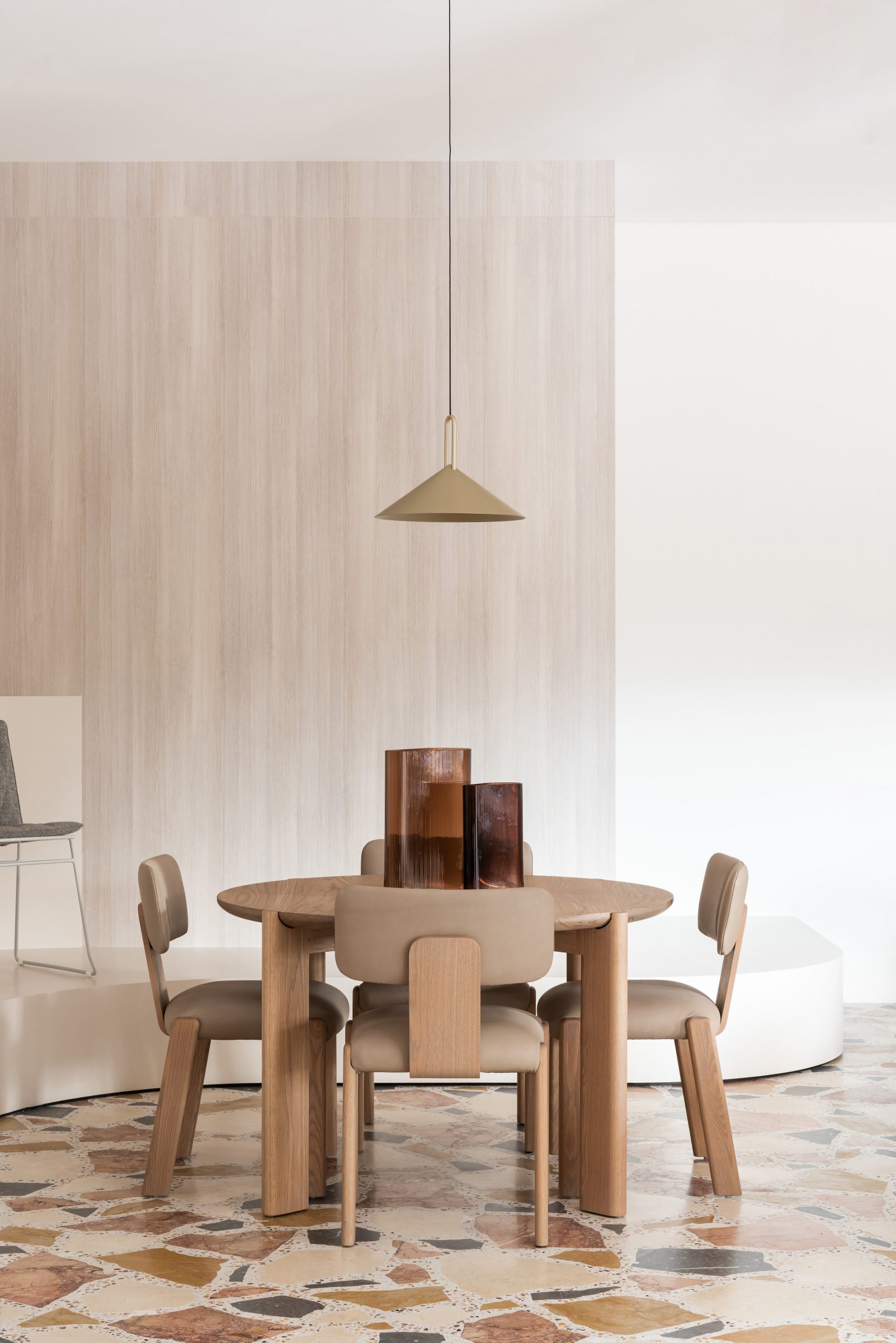 Jardan dining room with wooden table, modern chairs, pendant light, and decorative vases on terrazzo floor.