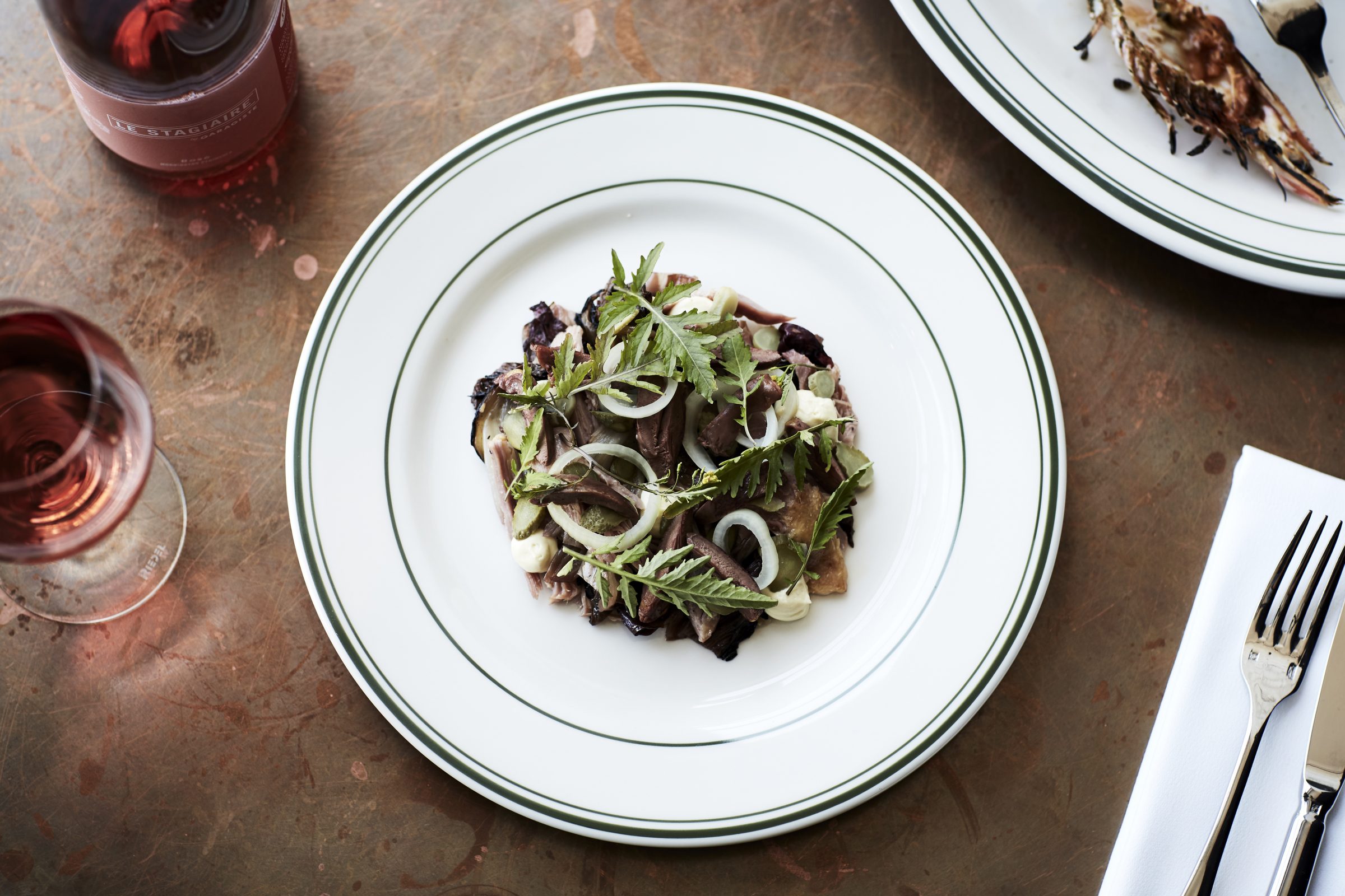 Plate of gourmet salad and wine from Marion dining collection on rustic table setting.