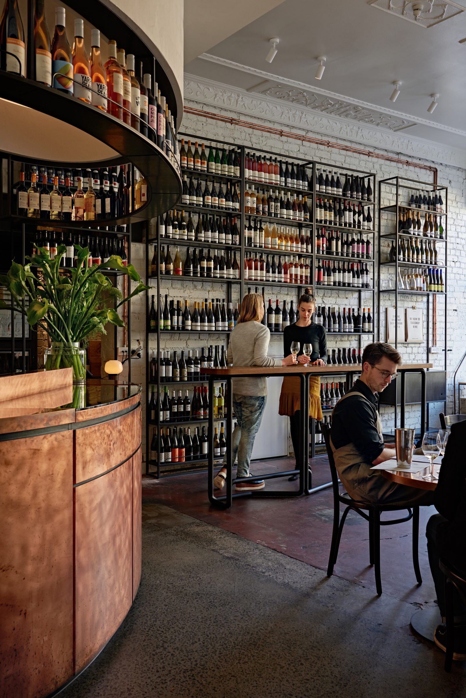Wine bar interior with patrons seated and standing amidst shelves of bottles Marion.