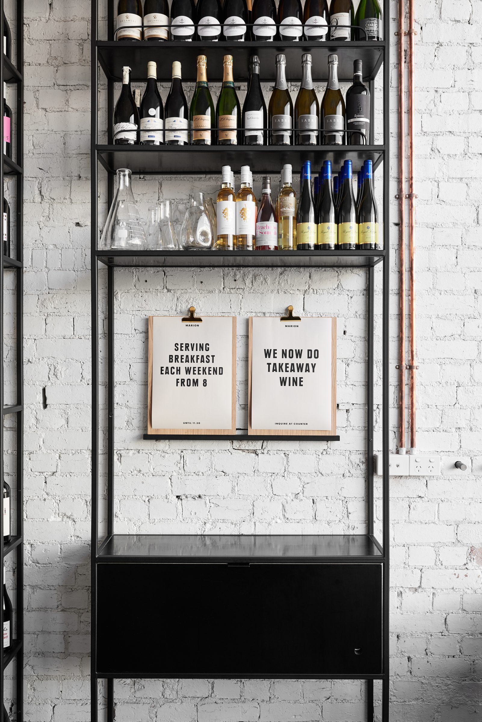 Wine display with breakfast and takeaway wine signs from Marion against a white brick wall.