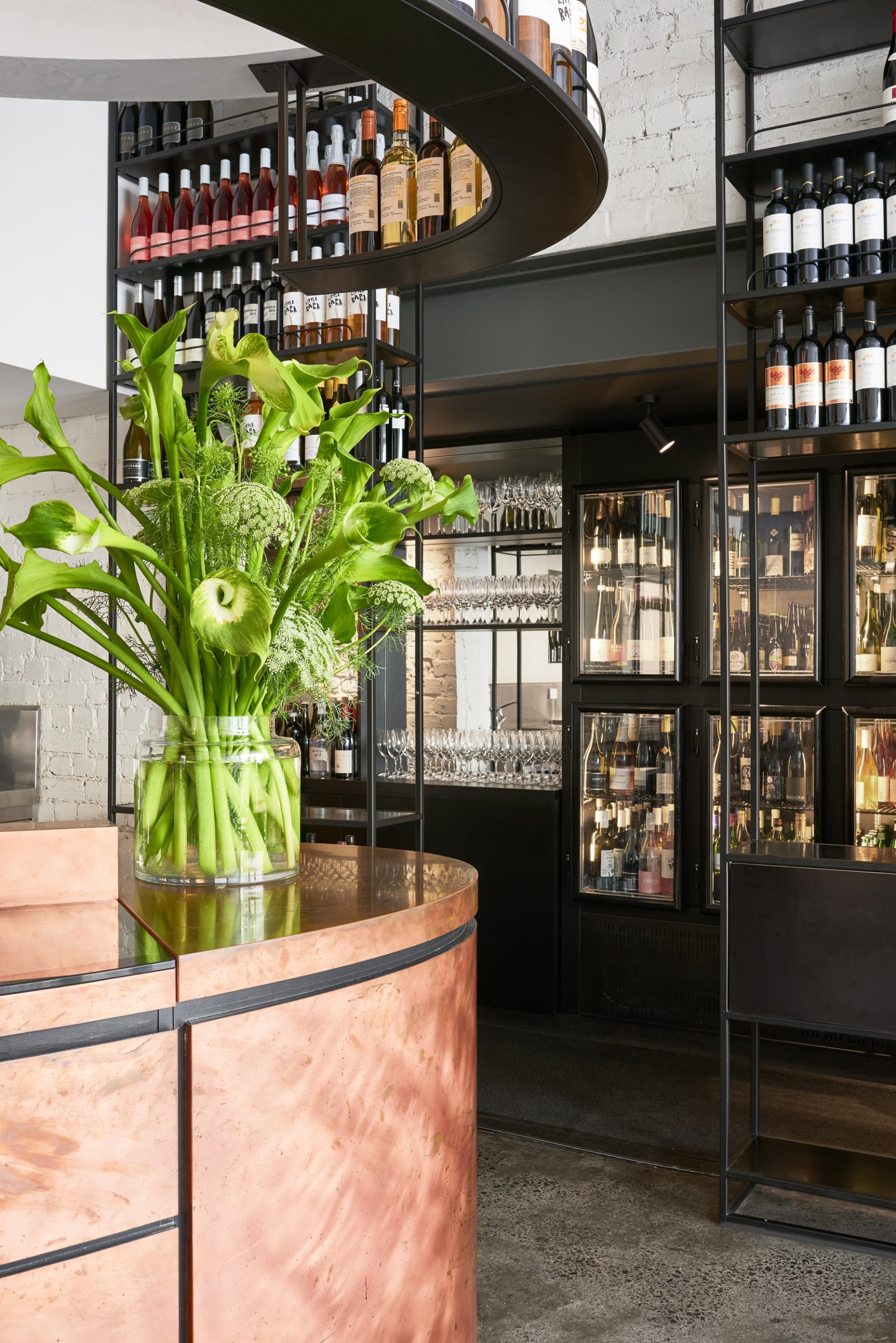 Modern bar interior with wine display and green floral arrangement, part of Marion.