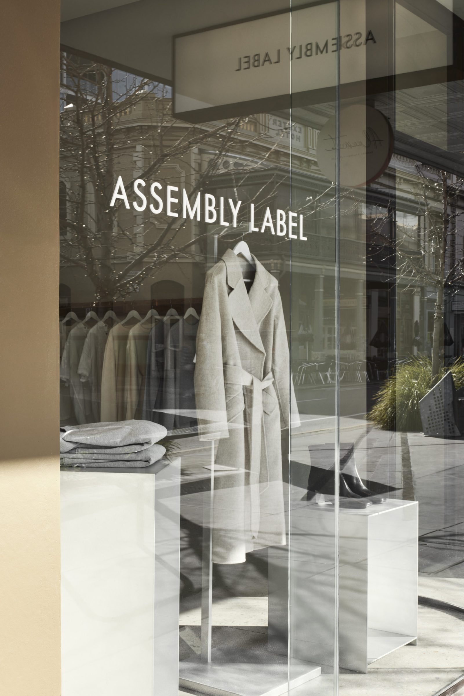 Storefront display of Assembly Label, Adelaide featuring stylish coats and folded clothing.