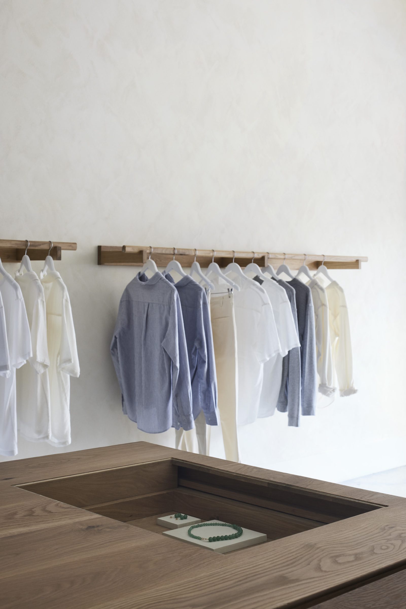 Assembly Label, Adelaide: minimalist clothing display with shirts and jewelry on wooden fixtures.
