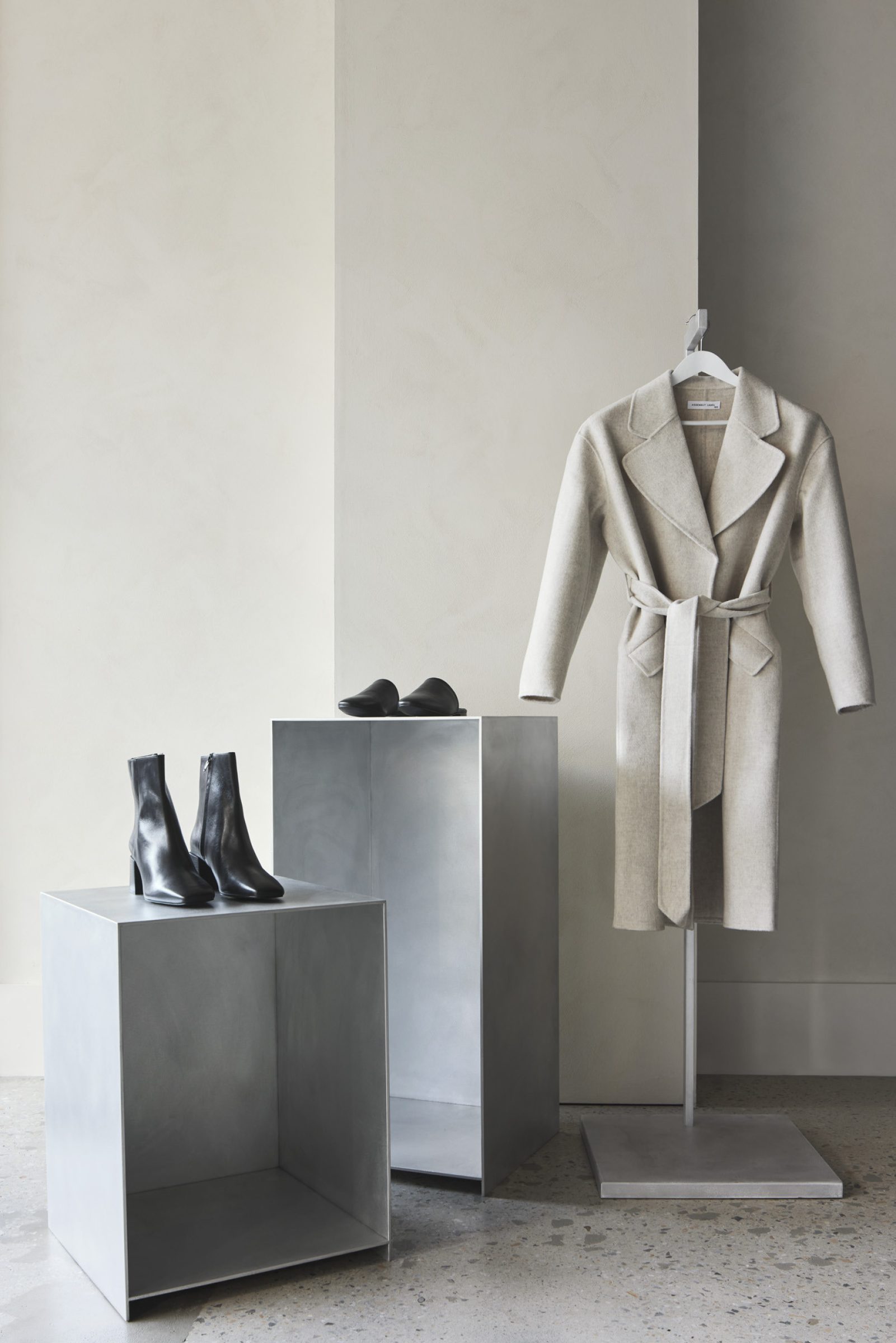 Assembly Label display featuring a beige coat and black leather boots on metal stands.