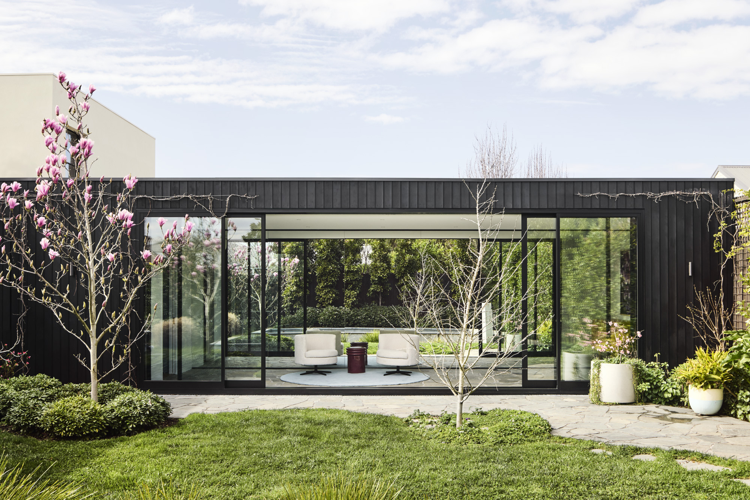 Modern glass-walled building surrounded by lush garden, part of Day House.