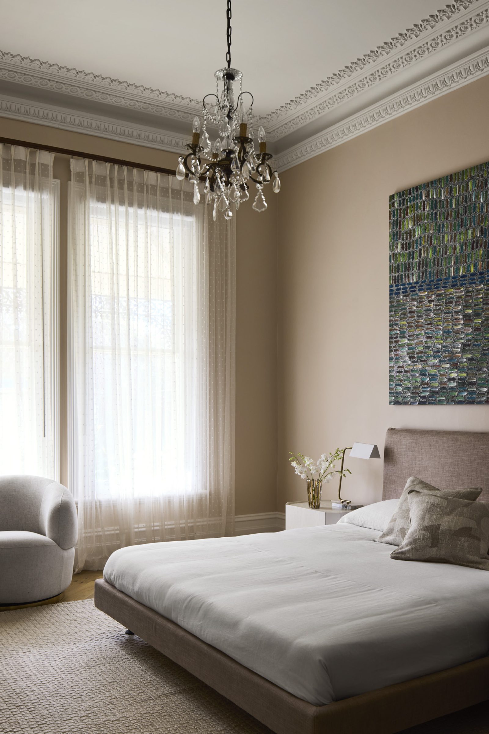Elegant bedroom interior from "Day House" featuring a chandelier, artwork, and soft furnishings.