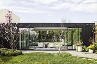Modern glass-walled building surrounded by lush garden, part of Day House.