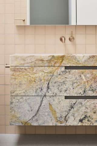 Marble bathroom vanity with gold fixtures from Day House, featuring beige tiled walls.