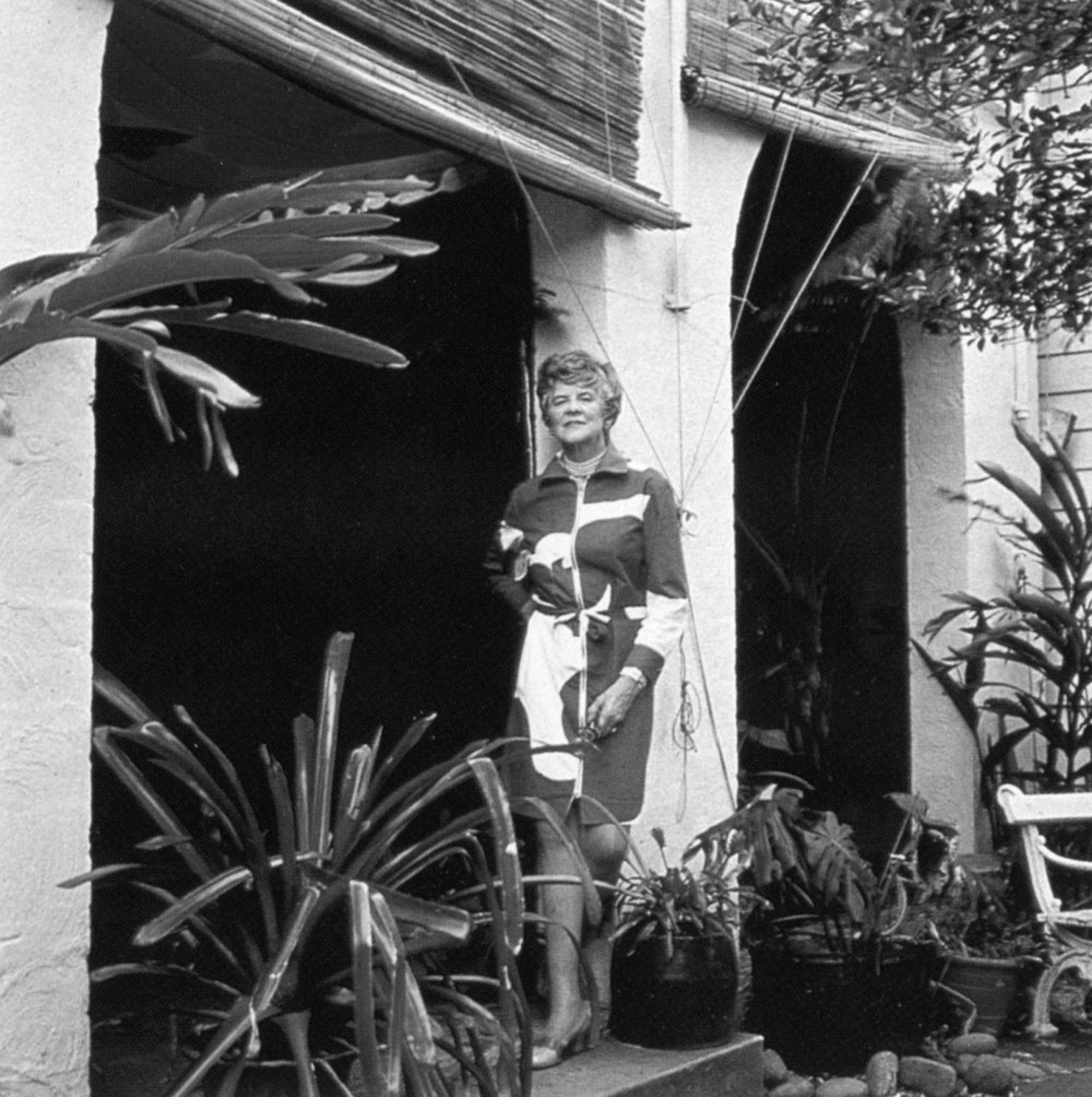 Woman in patterned dress standing in a garden doorway for Jardan Sydney.