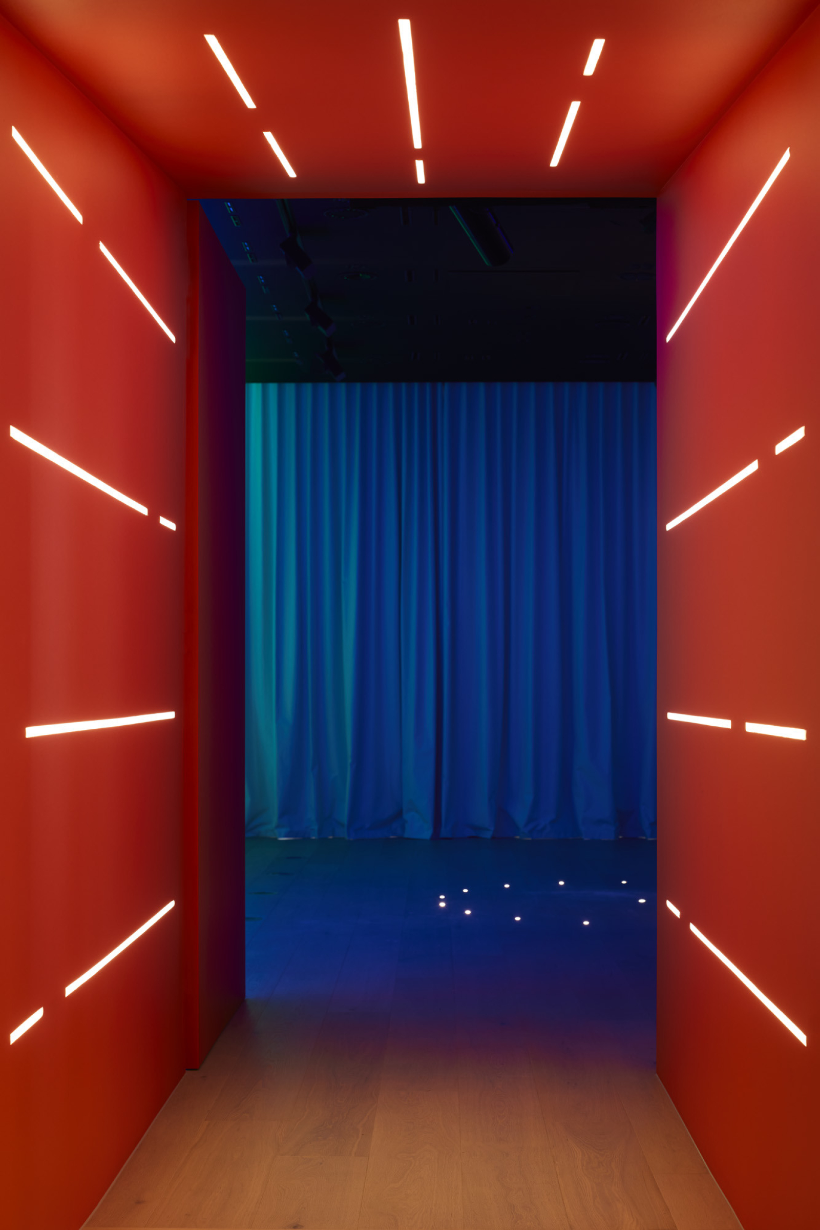 "Lux-Fx installation features a red corridor with linear lights and a blue curtain backdrop."