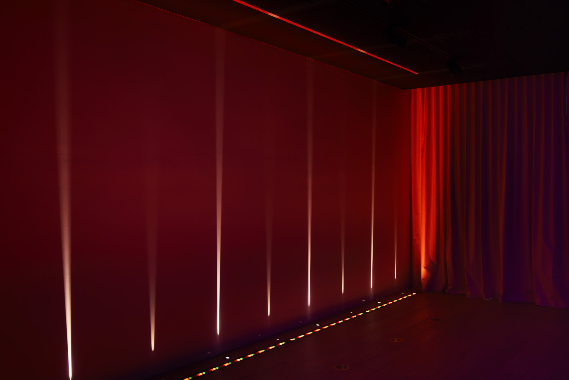 Red-lit wall with vertical light beams, part of Lux-Fx's atmospheric lighting display.