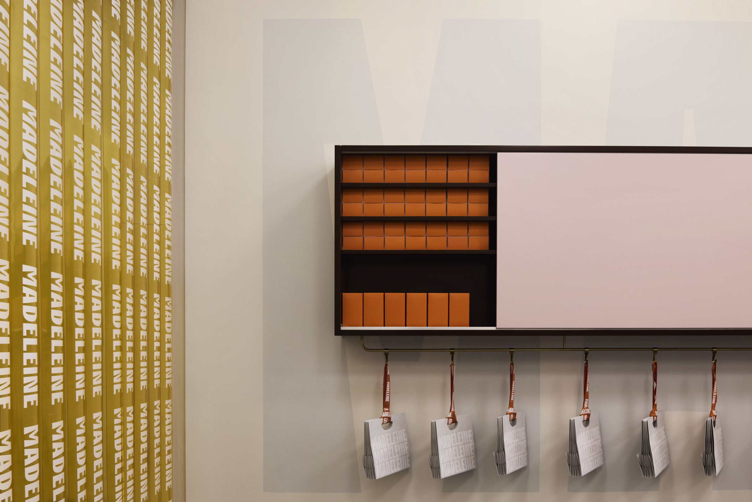Shelf with orange boxes and hanging bags, featuring "Madeleine de Proust" design elements.