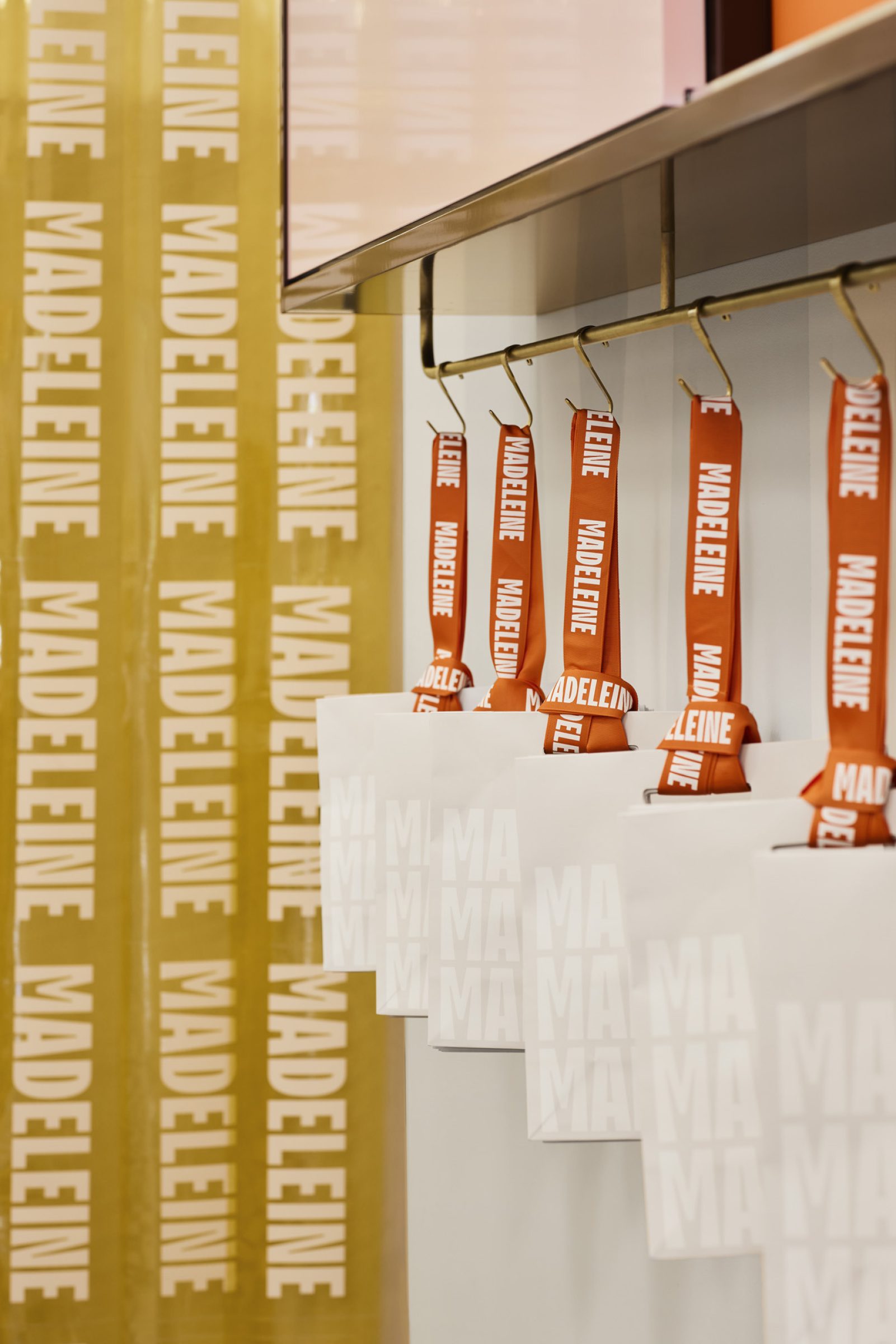 White bags with "Madeleine" ribbons hang in a row, showcasing "Madeleine de Proust".