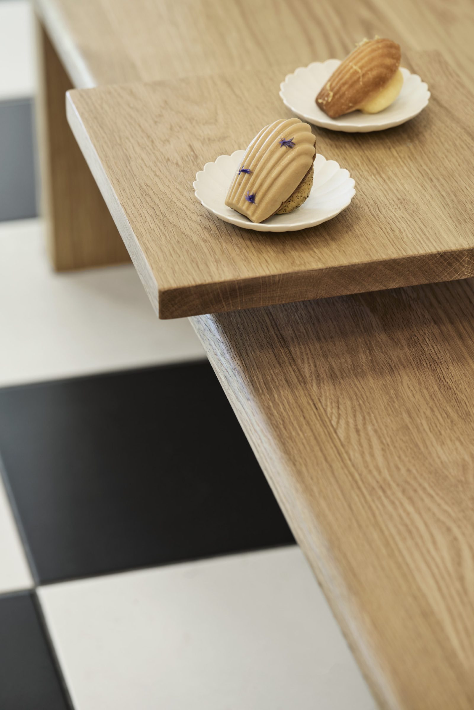 Madeleine de Proust features elegant madeleines on a wooden table with checkered flooring.