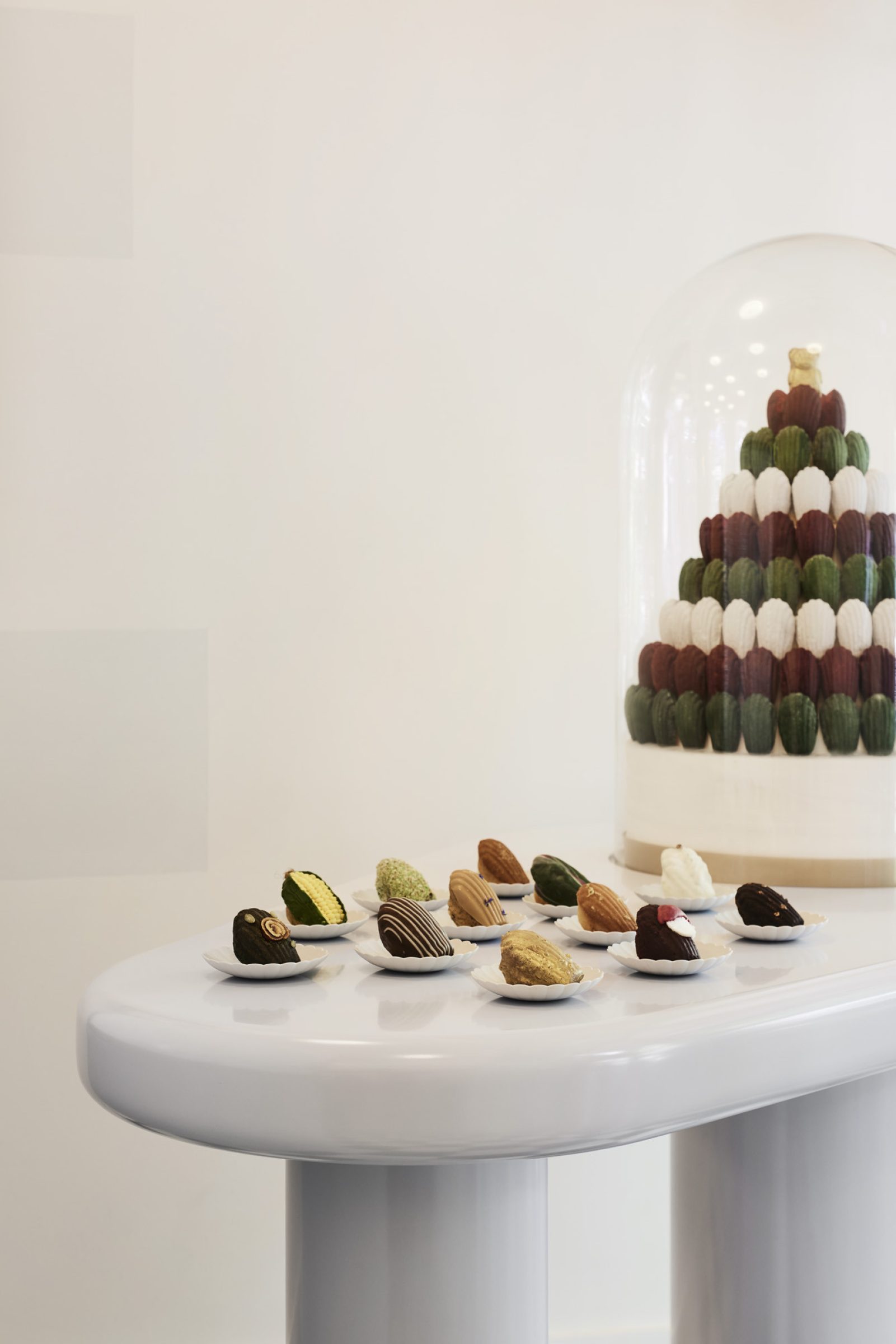 Assorted madeleines displayed on a table, with a pyramid of madeleines under a glass dome.