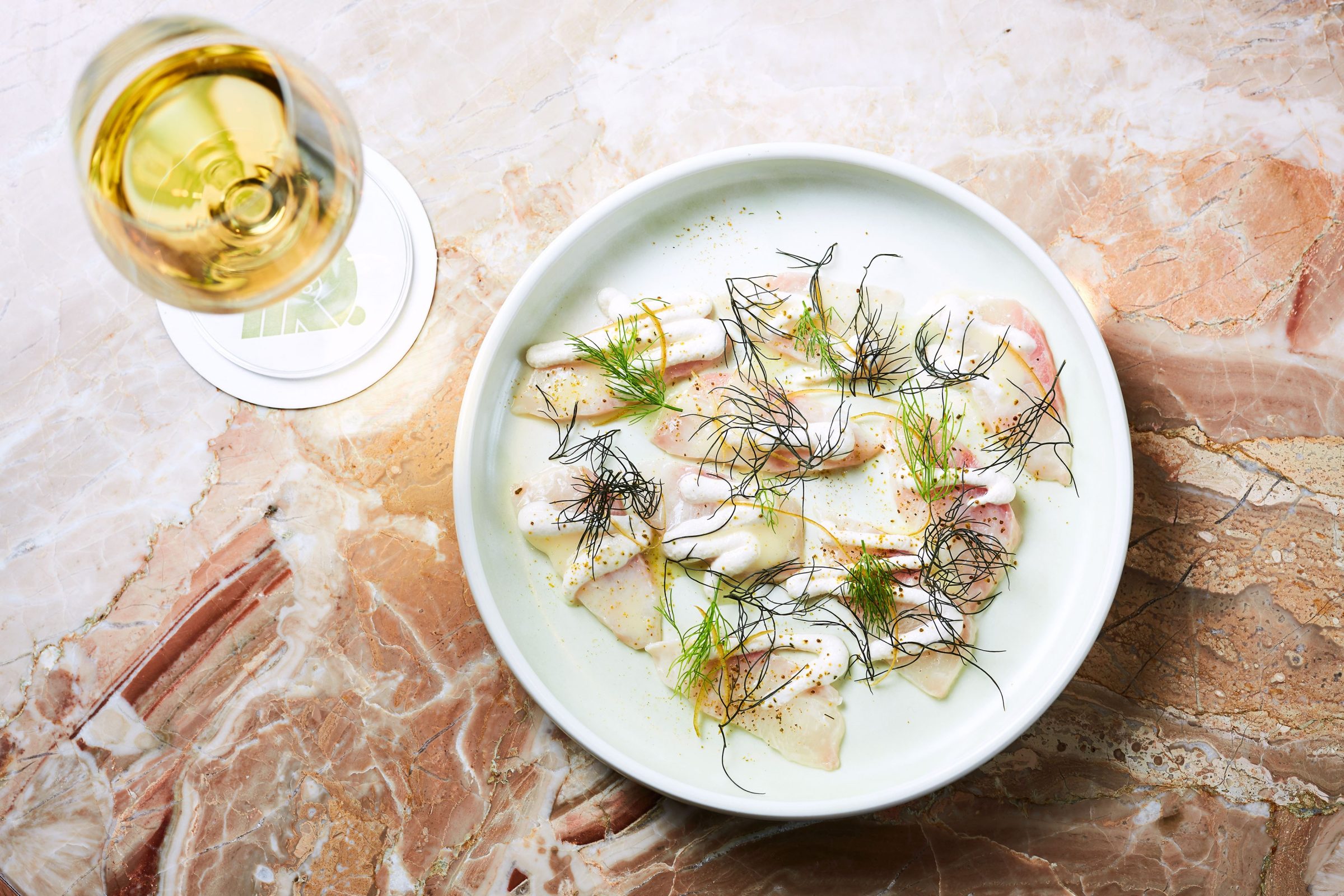 Elegant seafood dish with herbs and a glass of white wine on marble at Prince Dining Room.