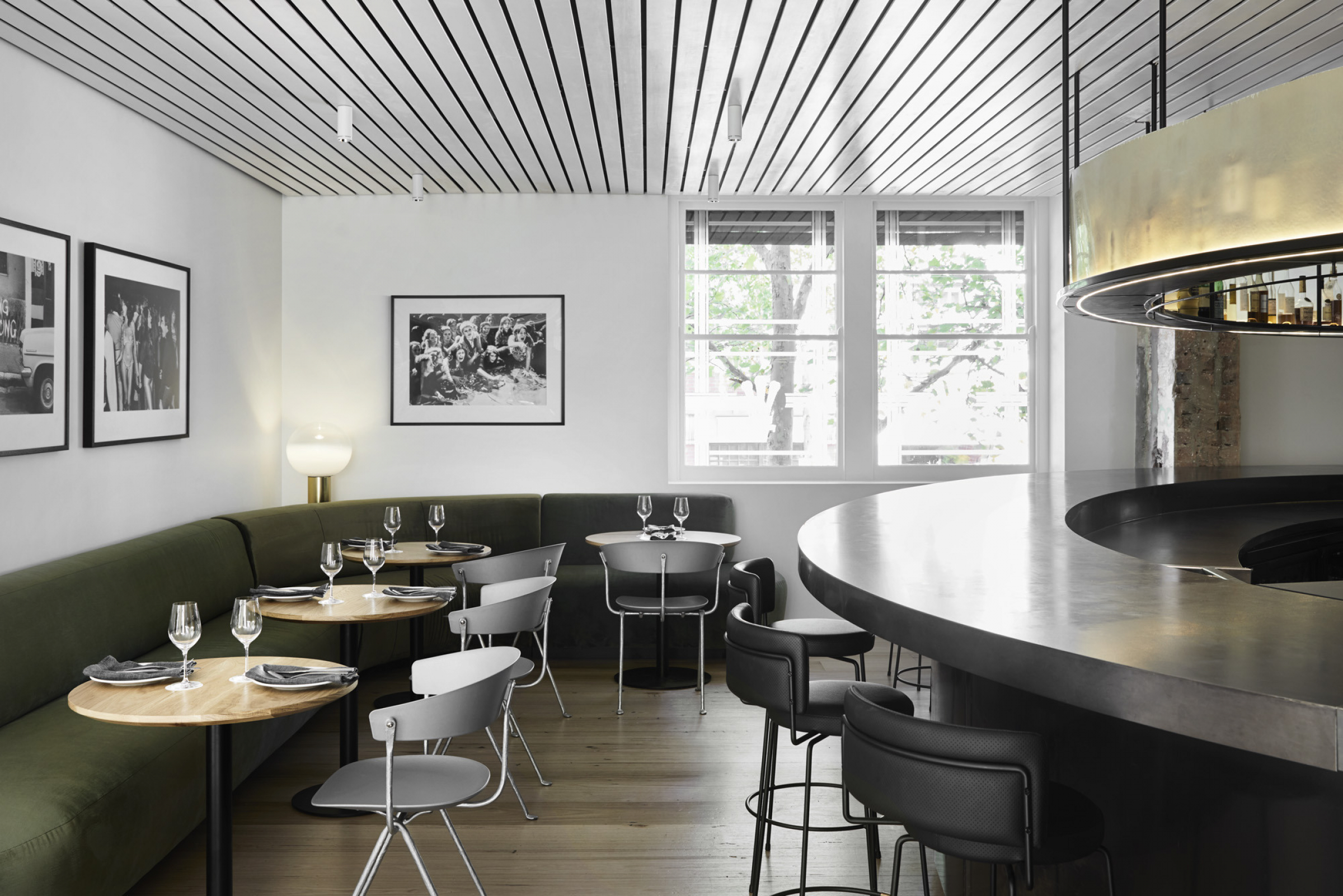 Modern restaurant interior with curved bar, green booths, minimalist tables, and large windows.