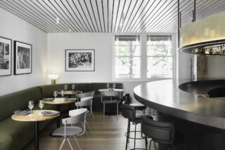 Modern restaurant interior with curved bar, green booths, minimalist tables, and large windows.